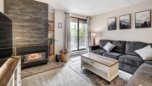 Een woonkamer met een open haard, een bank, een salontafel en een groot raam met uitzicht op bomen.