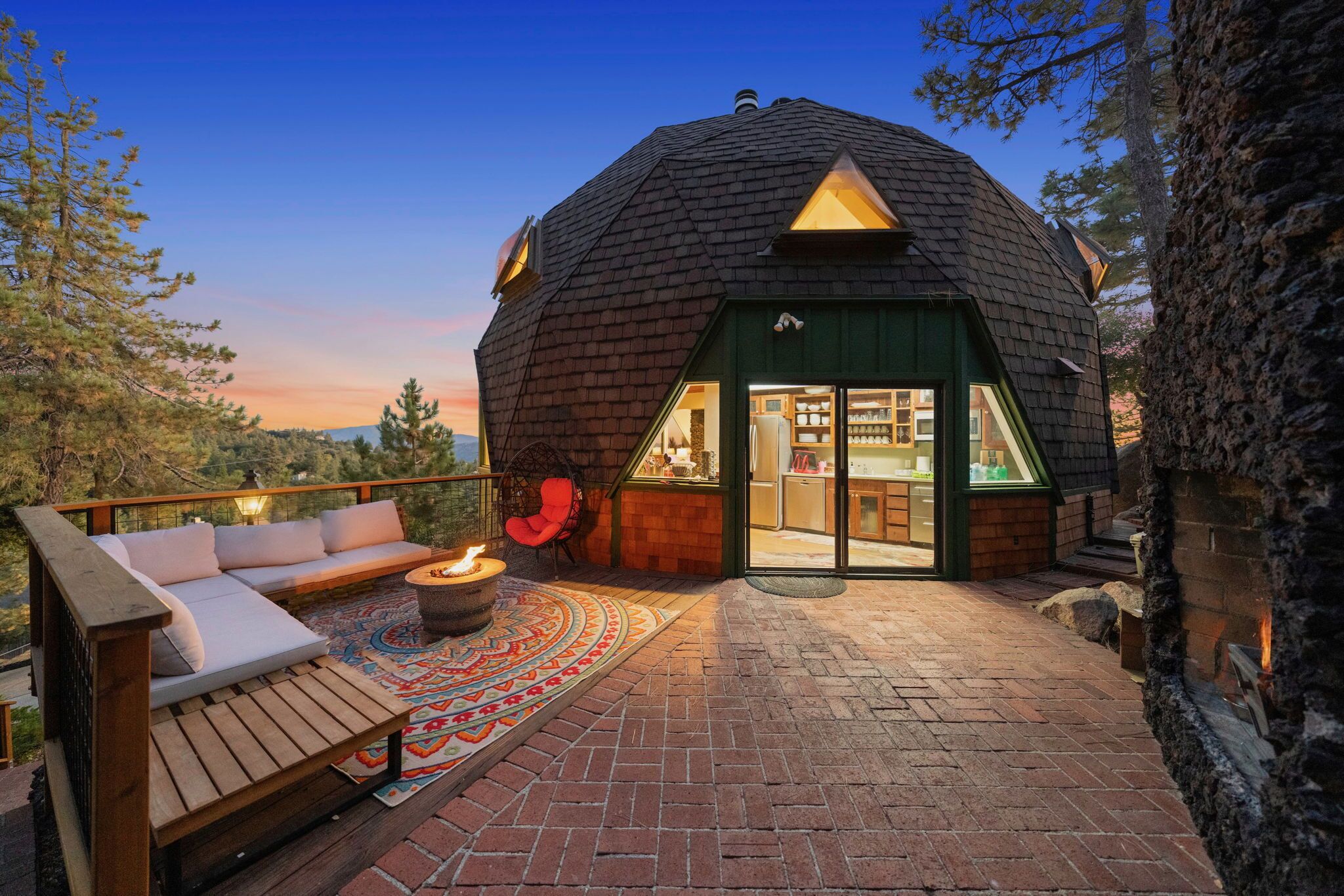 A geodesic dome structure with a patio area featuring a sofa, a fire pit, and a rug.