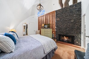 A bedroom with a stone fireplace, a bed with a patterned bedspread, and a wooden wardrobe. - Dramatic Geodesic Dome with amazing views, AC, spa and walk to town cold tub (Idyllwild)