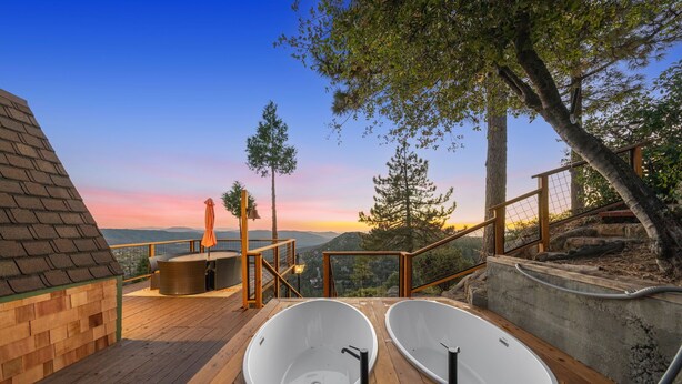Eine Holzterrasse mit zwei weißen Badewannen, einer Holzbank und einem Tisch mit orangefarbenem Sonnenschirm.