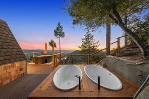 A wooden deck with two white tubs, a wooden bench, and a table with an orange umbrella. - Dramatic Geodesic Dome with amazing views, AC, spa and walk to town cold tub (Idyllwild)