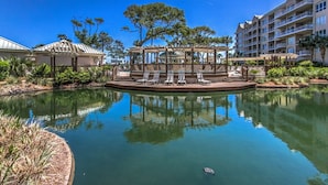 Un área de piscina tranquila con sillones de descanso, un pabellón y vistas despejadas a un edificio de hotel de varios pisos.