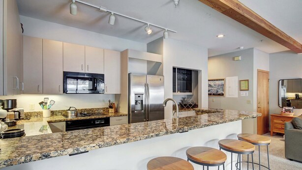 A modern kitchen with granite countertops, stainless steel appliances, and a bar area with stools. - Affordable Ski In/Out Mountain Oasis: Recent Updates, Easy Walk to Main St (Breckenridge)
