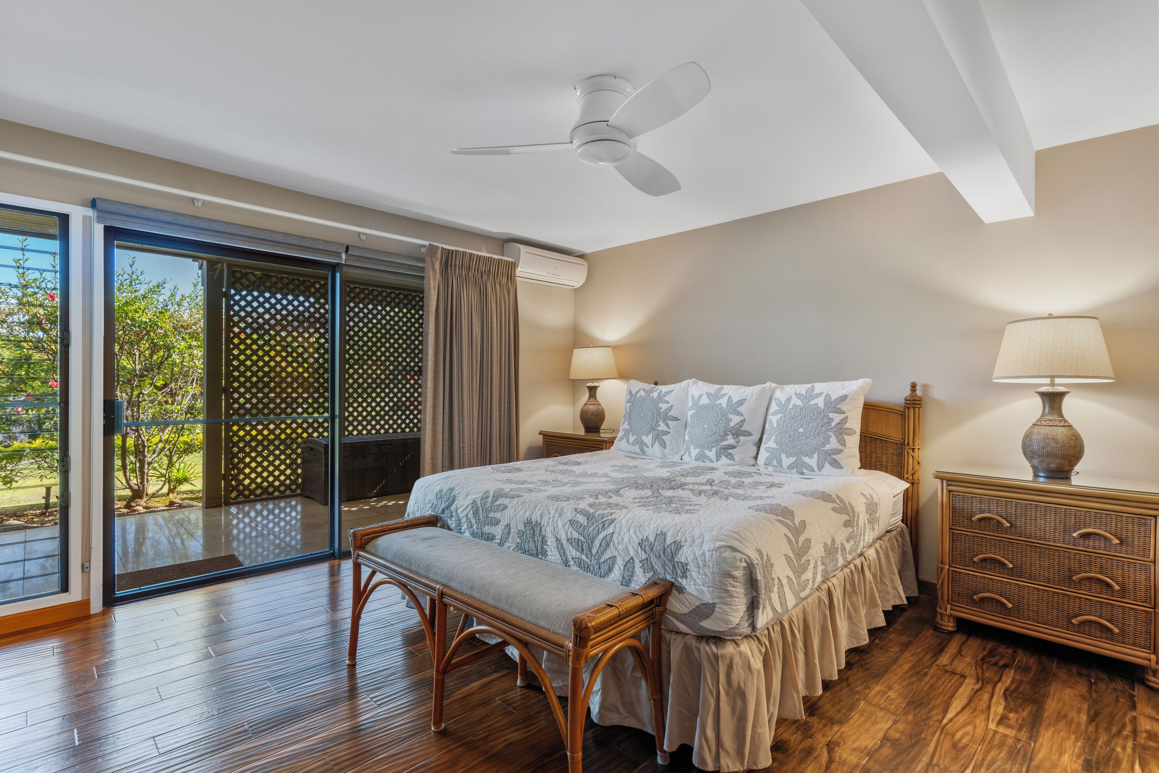 A bedroom with a bed, bedside tables, a bench, a ceiling fan, and a sliding glass door leading to an outdoor area.