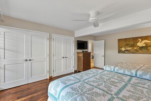 Ein Schlafzimmer mit zwei Betten, einem Deckenventilator, einem Fernseher und einem Bild an der Wand.