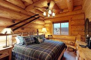A log cabin bedroom with a bed, a desk, a chair, a lamp, and a window.