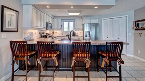 A modern kitchen with white cabinets, a central island with bar stools, and a stainless steel refrigerator.