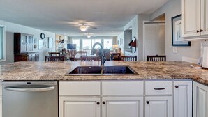 A kitchen with a granite countertop, white cabinets, a built-in dishwasher, and a ceiling fan.