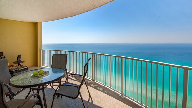 A balcony with a table and chairs, overlooking a clear blue sea. - Affordable!Luxurious!BeachFront!TopFlrCondo!ReservedParking!Beach Service Included (Panama City Beach)