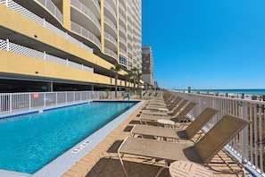 A poolside area with a clear blue pool, lounge chairs, and a view of the ocean.