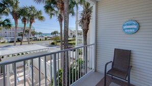 A balcony with a chair, palm trees, and a sign that says "WHEREVER WE ARE THAT IS HOME".