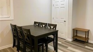 Un comedor con una mesa rectangular y seis sillas, una puerta blanca y un pequeño banco de madera.