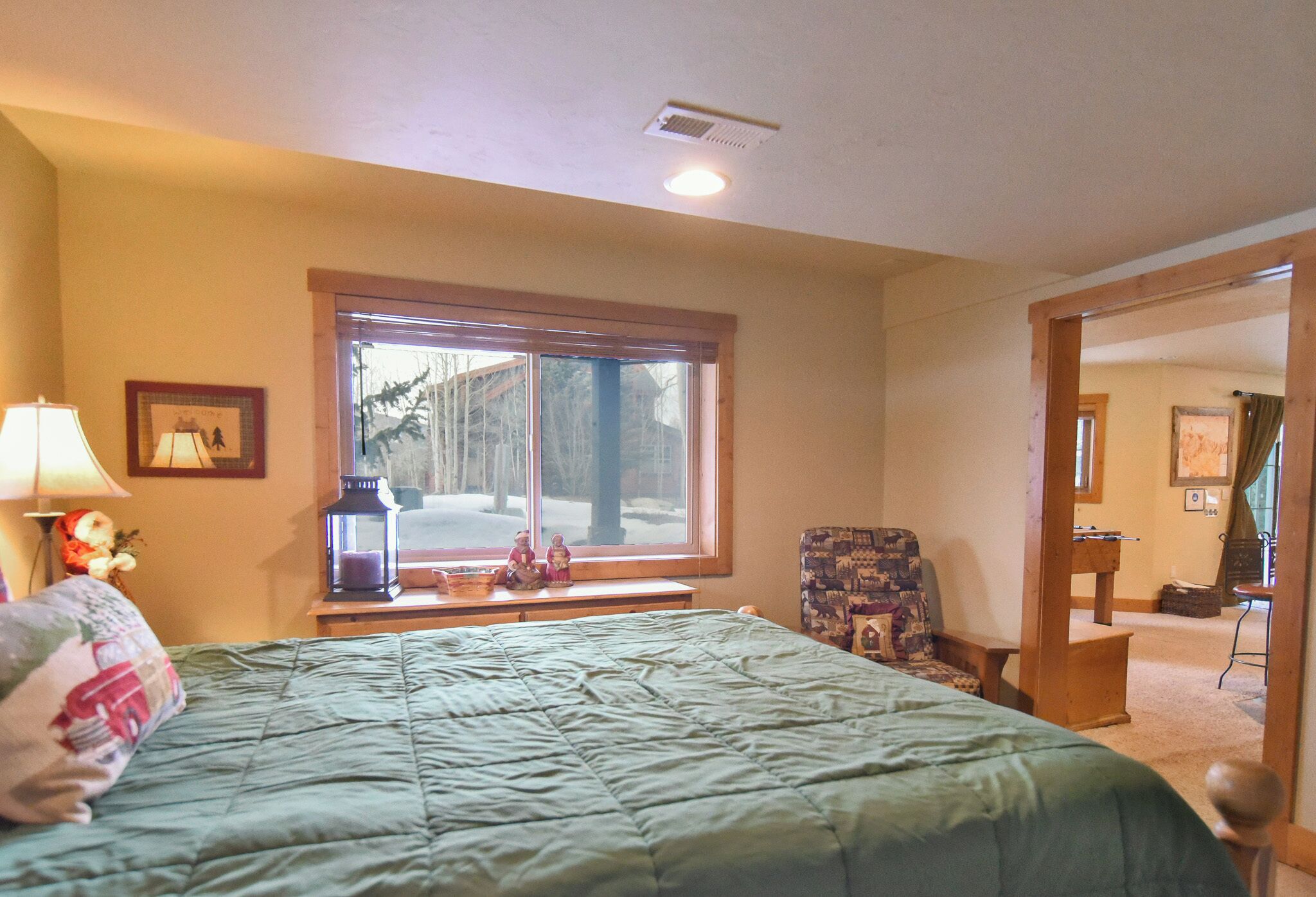Une chambre avec un grand lit, une fenêtre donnant sur les arbres, une chaise et une lampe.