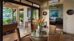 Ein modernes Wohnzimmer mit Glastisch, Korbmöbeln und Blick ins Freie.