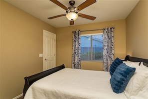 Une chambre à coucher avec un lit, un ventilateur de plafond et une fenêtre ornée de rideaux à motifs.