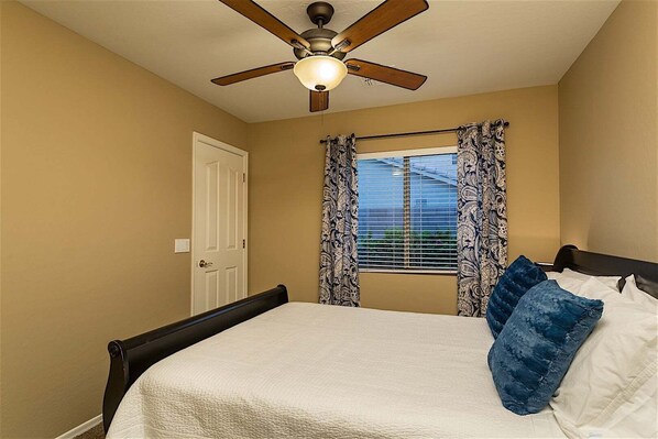 A bedroom with a bed, a ceiling fan, and a window with patterned curtains.