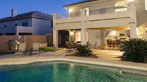 Une maison à deux étages avec une piscine, un espace repas extérieur et un barbecue.
