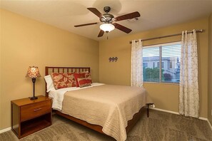 A bedroom with a bed, a nightstand, a lamp, a ceiling fan, and a window with curtains.