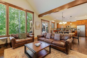 A spacious living room with leather sofas, a coffee table, and large windows with blinds.
