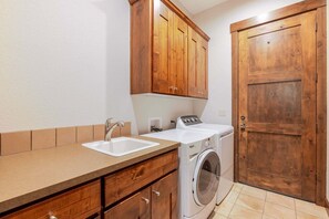 A laundry area with a washing machine, a sink, wooden cabinets, and a door.