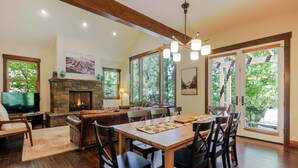 A spacious living area with a fireplace, dining table, and large windows offering a view of the outdoors. - Points West - Close to Bend w/Hot Tub AC, Golf, and Mt Bachelor, 4 Suites (Bend)