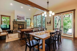 A spacious living area with a fireplace, dining table, and large windows offering a view of the outdoors.
