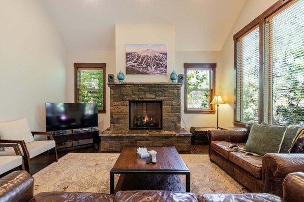 A living room with a stone fireplace, a television, leather furniture, and large windows with blinds. - Points West - Close to Bend w/Hot Tub AC, Golf, and Mt Bachelor, 4 Suites (Bend)