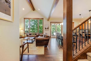 A spacious living area with a wooden staircase, large windows, and a dining area.