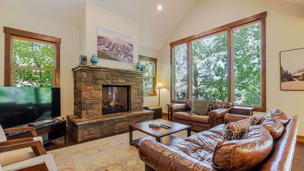 A living room with a stone fireplace, leather sofa, and large windows. - Points West - Close to Bend w/Hot Tub AC, Golf, and Mt Bachelor, 4 Suites (Bend)
