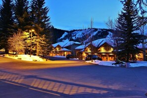 A row of log cabin-style buildings with snow-covered roofs, surrounded by tall evergreen trees and a mountain backdrop. - Indulge in Luxury - Perfect for Groups with Private Hot Tub & Posturepedic Beds! (Park City)