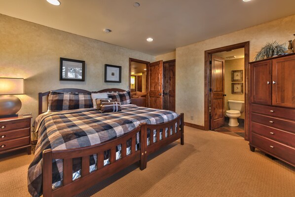 A bedroom with a large bed, wooden headboard, a nightstand, a dresser, and a door leading to another room. - Indulge in Luxury - Perfect for Groups with Private Hot Tub & Posturepedic Beds! (Park City)