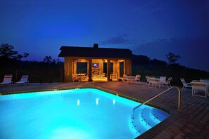 A swimming pool with a sunken hot tub, lounge chairs, and a covered seating area with a TV.