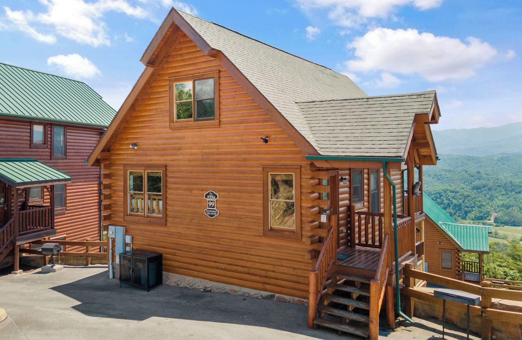 A log cabin with a porch, a staircase, and a view of the mountains.