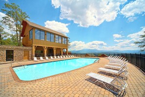A pool area with lounge chairs and a building with large windows. - Stunning Mountain Views | Game Room | Pet Friendly | Hot Tub | WiFi (SEVIERVILLE)