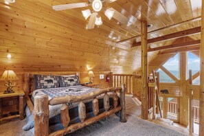 A log cabin bedroom with a large bed, wooden ceiling, and a view through a balcony.