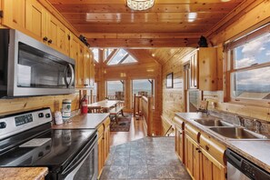 A modern kitchen with wooden cabinetry, a stainless steel stove, and a large window overlooking a scenic view. - Stunning Mountain Views | Game Room | Pet Friendly | Hot Tub | WiFi (SEVIERVILLE)