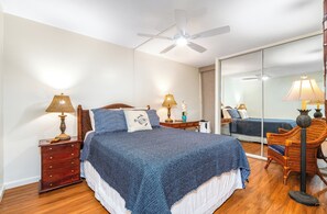 A bedroom with a large bed, wooden nightstands, a ceiling fan, and a mirror.