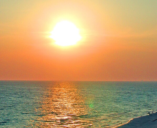 Atardecer sobre un mar tranquilo con una playa en primer plano.