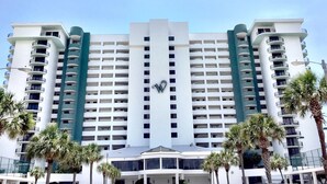 Een hotel met meerdere verdiepingen, een centraal atrium, balkons en palmbomen op de voorgrond.