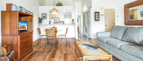 A spacious living area with a wooden coffee table, a grey sofa, and a dining table with wicker chairs.