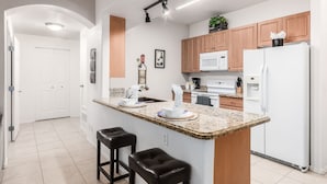 Eine moderne Küche mit Granit Arbeitsplatten, Holzschränken, einem weißen Kühlschrank und einer eingebauten Mikrowelle.