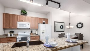 Eine moderne Küche mit Granit Arbeitsplatten, Holzschränken, einem weißen Kühlschrank und einem Essbereich mit einer Chandelier und Wanduhr.