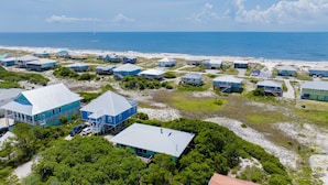A coastal area with multiple blue buildings, some with elevated structures, near a beach with a clear view of the ocean. - Gulf Views | Beach Access | Pet Friendly Coastal Bungalow (Gulf Shores)