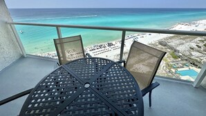 Ein Balkon mit Tisch und Stühlen mit Blick auf einen Strand und klares türkisfarbenes Wasser.