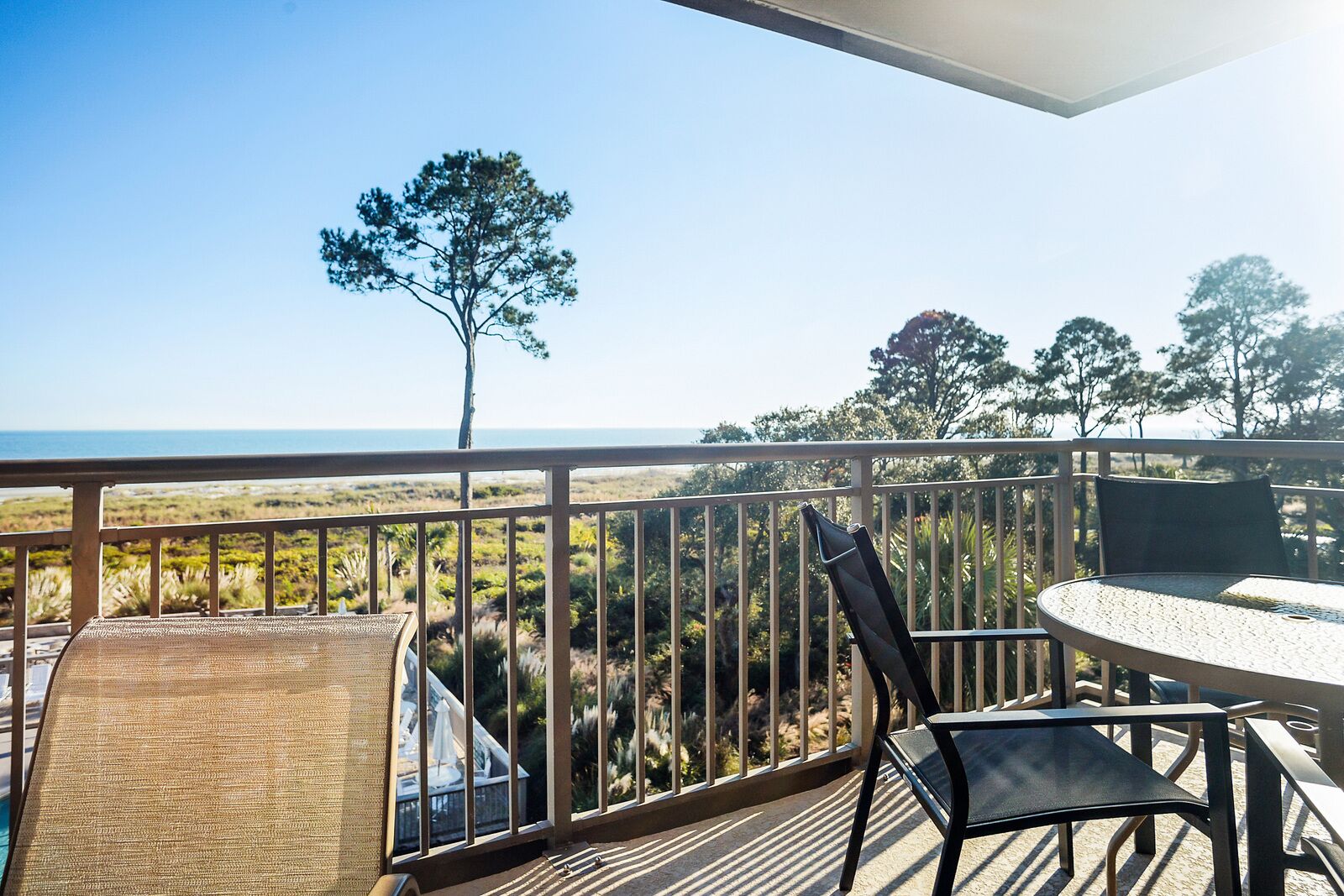 A balcony with a view of the ocean, a table, and chairs.