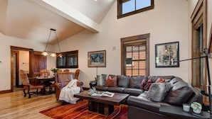 A spacious living room with a large sectional sofa, a dining area with wooden furniture, and a high ceiling with exposed beams.