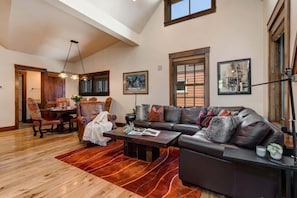 A spacious living room with a large sectional sofa, a dining area with wooden furniture, and a high ceiling with exposed beams.