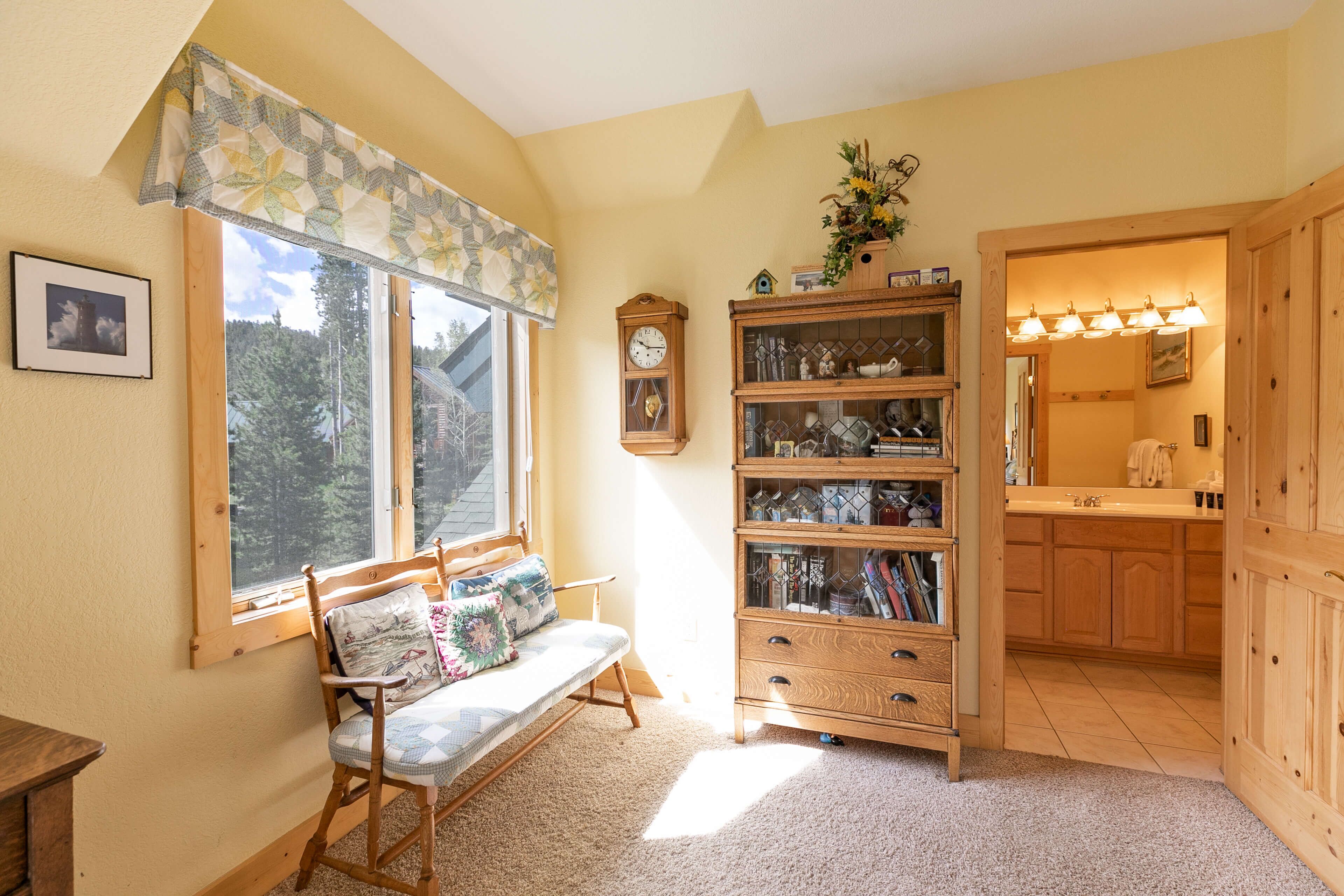 A cozy room with a wooden bench, a bookshelf, a clock, and a view of the outdoors.