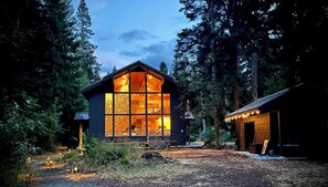 Una cabaña con amplias ventanas, fachada de madera y un bosque circundante.