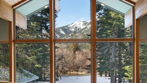 Una escalera de madera conduce a una habitación con ventanas amplias que dan a un paisaje nevado y árboles.